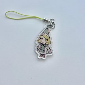May include: A clear acrylic charm with a cartoon illustration of a character in a green and white outfit and hat. The charm has a yellow lanyard attached with a silver clasp.