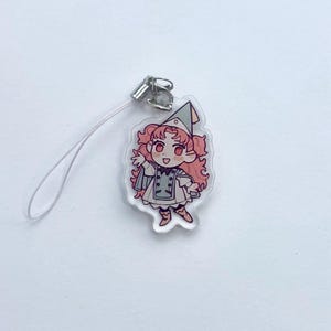 May include: A clear acrylic charm depicting a cartoon character with pink hair, a green hat, and a white and grey outfit. The charm has a silver clasp and a white lanyard. The character is smiling with arms outstretched.