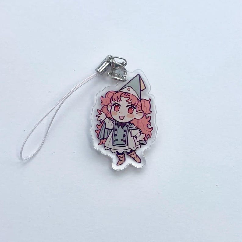 May include: A clear acrylic charm depicting a cartoon character with pink hair, a green hat, and a white and grey outfit. The charm has a silver clasp and a white lanyard. The character is smiling with arms outstretched.