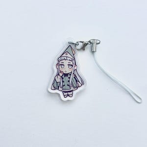 May include: A clear acrylic charm with a cartoon illustration of a character in a green and white outfit. The charm has a silver-coloured clasp and a white lanyard. The character has long white hair and is wearing a hat.
