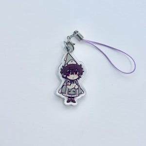 May include: A clear acrylic charm depicting a cartoon character with brown hair, dressed in a green and white outfit. It has a silver clasp and a purple lanyard. The character has a serious expression.