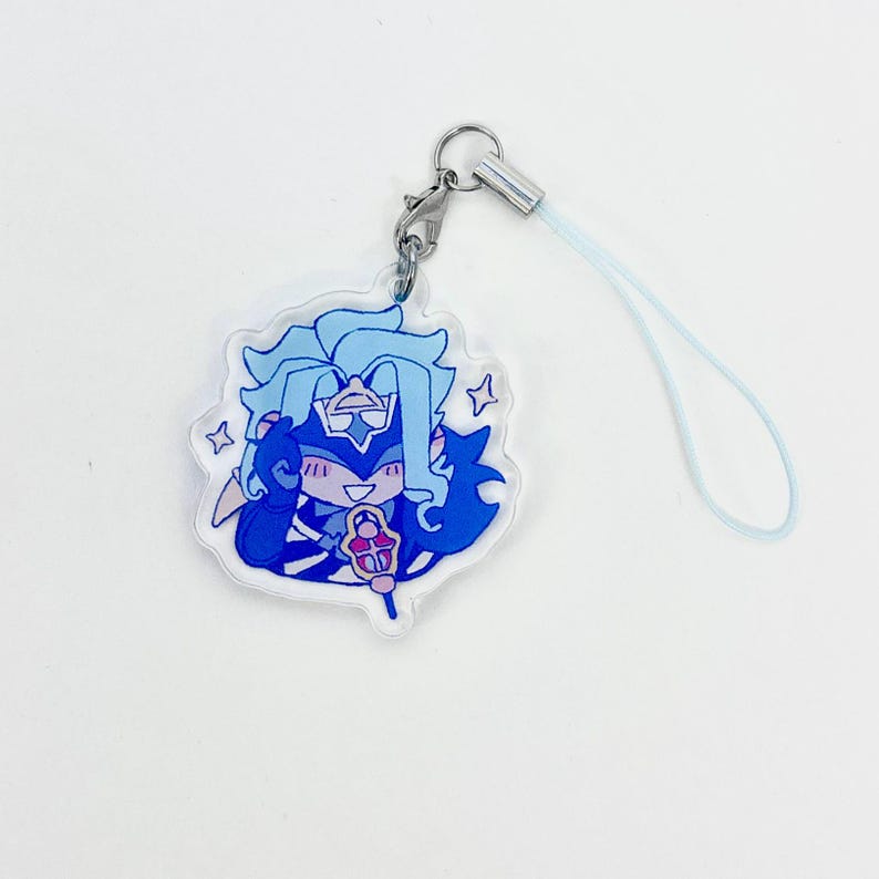 May include: A clear acrylic charm featuring a cartoon character with blue hair and clothing, holding a staff. The charm is attached to a silver clasp and a light blue lanyard. The character is surrounded by star shapes.