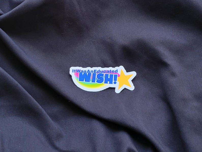 以下が含まれることがあります： 虹色の弧と黄色の星が付いた白いステッカー。ステッカーには「It Was An Educated WISH!」と書かれています。