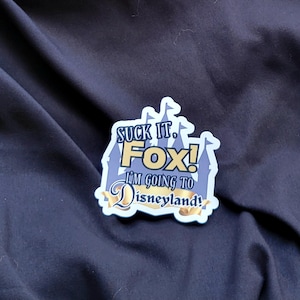 以下が含まれることがあります： 「Suck it. Fox! I'm going to Disneyland!」と書かれた青と金のステッカー。ステッカーは城の形をしています。