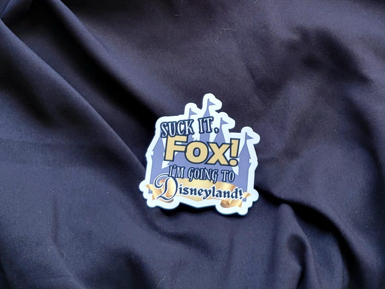 以下が含まれることがあります： 「Suck it. Fox! I'm going to Disneyland!」と書かれた青と金のステッカー。ステッカーは城の形をしています。