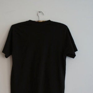 May include: A solid black t-shirt hanging on a metal hanger against a white wall. The short-sleeved shirt is made of a soft material and is a basic wardrobe staple.