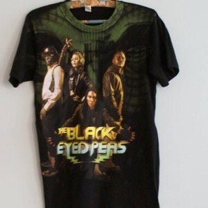 May include: Black t-shirt featuring a graphic of The Black Eyed Peas band members. The design includes the band's name in a stylized font with a green and yellow color scheme. The shirt has a green and black tie-dye pattern on the top.