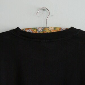 K&ouml;nnte beinhalten: Schwarzes Langarm-T-Shirt, das an einem Kleiderb&uuml;gel h&auml;ngt, mit einem floral gemusterten Stoff darunter.