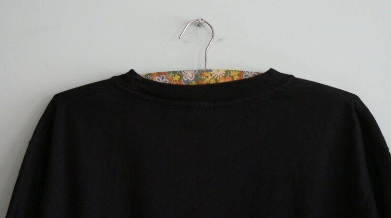 K&ouml;nnte beinhalten: Schwarzes Langarm-T-Shirt, das an einem Kleiderb&uuml;gel h&auml;ngt, mit einem floral gemusterten Stoff darunter.