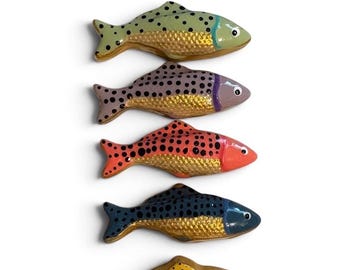 May include: A set of five decorative fish figurines arranged vertically. Each fish features a distinct solid color head and tail with black polka dots, paired with a textured, metallic gold midsection. The colors include light green, purple, orange, blue, and yellow.