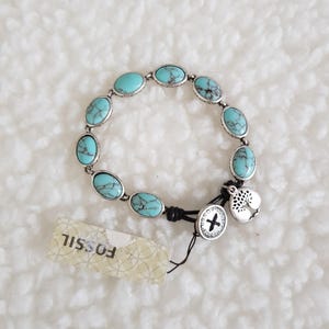 May include: A Fossil bracelet with oval turquoise stones set in silver-tone metal. The bracelet has a black cord closure and a charm with a tree design. A Fossil tag is attached.