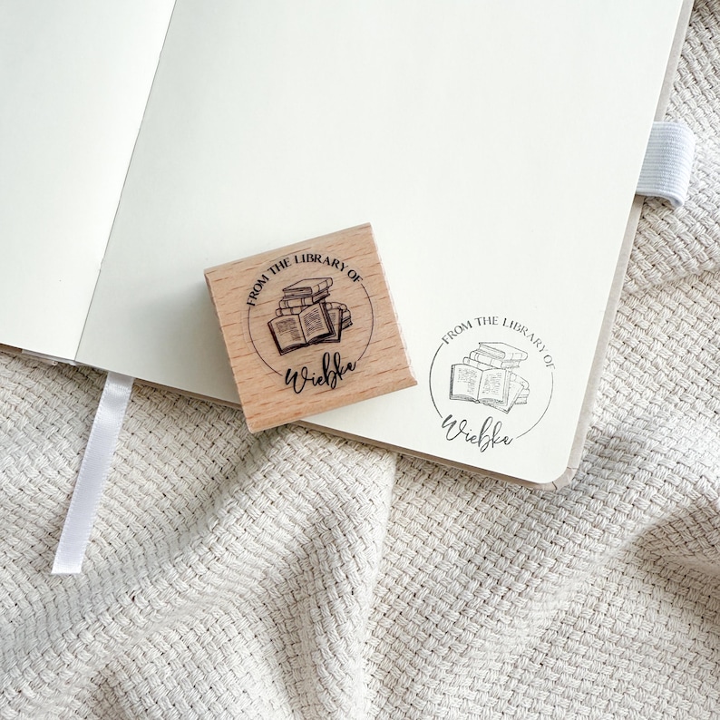 Ein Holzstempel mit dem Motiv "from the shelf of" und dem Namen als Personalisierung. In der Mitte des Stempelmotivs ist ein Stapel Bücher zu sehen.