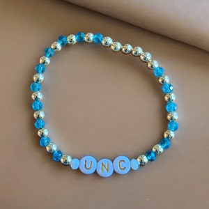 May include: A blue and silver beaded bracelet with the letters UNC spelled out in gold on white beads.