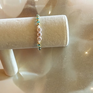 May include: A gold and turquoise beaded bracelet with white letter beads spelling out "UNC".