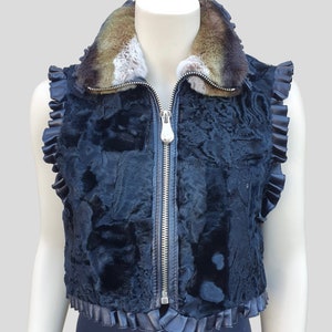 Può includere: Un gilet di pelliccia nero con chiusura a zip e colletto di pelliccia marrone. Il gilet ha volant sui bordi.