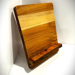 May include: A wooden cookbook stand with a warm, natural wood grain finish. The stand is angled for easy viewing and features a ledge to hold a book or tablet. The stand is approximately 12 inches tall and 9 inches wide.