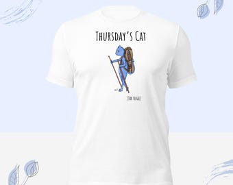 May include: A white short-sleeve t-shirt featuring a graphic of a blue cat hiking with a brown backpack and walking sticks. The text above the cat reads "Thursday's Cat" and the text below the cat reads "(FAR TO GO)" in black lettering.