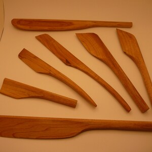 May include: A set of eight wooden tools, probably for pottery or sculpting, with various shapes and sizes. The tools are made of light brown wood and have smooth, rounded edges.