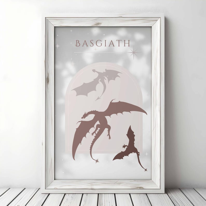 May include: A white framed print with the word "BASGIATH" in pink lettering. The print features three silhouettes of dragons in shades of pink and brown against a white background.