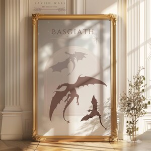 May include: A gold framed print with the word "BASGIATH" in a light brown font. The print features three silhouettes of dragons in shades of brown and gray against a light blue background.