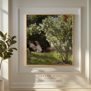 Peut inclure: Une peinture représentant une femme assise sur une chaise blanche dans un jardin, en train de lire un livre. Le jardin est rempli de fleurs blanches et de feuillage vert. La peinture est encadrée d'or.