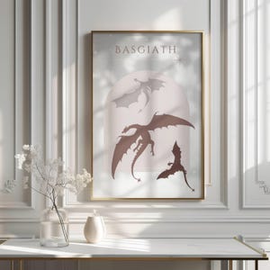 May include: A printable art print with a light pink background featuring three black silhouettes of dragons with the word "Basgiath" at the top.