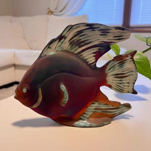 May include: A decorative glass fish figurine in shades of burgundy, brown, and teal. The fish has detailed fins and a textured body, with a small, round eye. The figurine is a unique home decor item.