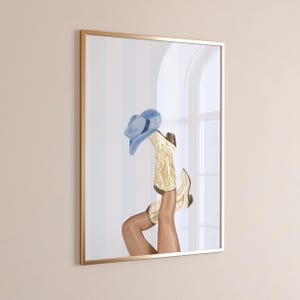 May include: A framed wall art print featuring a blue cowboy hat resting on a pair of cream-colored western boots with intricate stitching. The boots are positioned in an upward, angled orientation, showcasing the detailed embroidery on the leather.