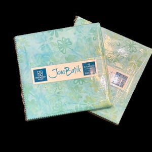 May include: Two stacks of fabric squares wrapped in clear plastic, labeled Java Batik by Maywood Studio. Each stack contains 42 charms measuring 5 inches square. The fabric features a light blue and green floral pattern with a watercolor effect.