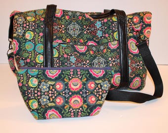 May include: A large tote bag and a matching smaller pouch featuring a dark green fabric base with a dense, colorful floral pattern in shades of pink, teal, yellow, and white. The tote has black faux leather handles and a detachable black shoulder strap.