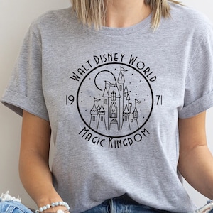 Puede incluir: Una camiseta gris con un gr&aacute;fico en blanco y negro del castillo de Cenicienta. El gr&aacute;fico incluye el texto "Walt Disney World" y "Magic Kingdom" con los a&ntilde;os "1971" a cada lado del castillo.