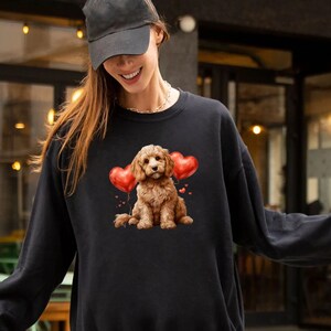 May include: A black sweatshirt featuring a brown and white dog holding red heart-shaped balloons. The dog is wearing a red collar.