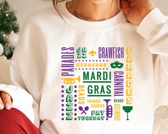 May include: White sweatshirt with a purple and green design featuring the words "Mardi Gras", "Carnival", "Crawfish", "French Quarter", "Fat Tuesday", "Beads", "Jazz", and "Parades".