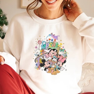 May include: White sweatshirt with a colorful graphic of Mickey Mouse and friends at Epcot. The graphic includes a Mickey Mouse ear hat, a lollipop, and the word "Epcot".