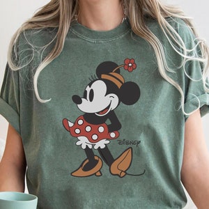 May include: A green t-shirt with a vintage-style image of Minnie Mouse wearing a red polka dot dress and a flower on her head. The text "DISNEY" is printed on the shirt.