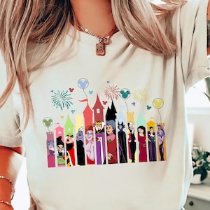 Puede incluir: Camiseta color crema con un gr&aacute;fico colorido de villanos de dibujos animados frente a un castillo. El gr&aacute;fico incluye fuegos artificiales y globos. La camiseta es una prenda casual para el d&iacute;a a d&iacute;a.