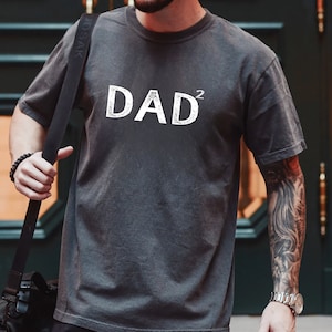 Pode incluir: Uma camiseta cinza com a palavra "DAD" e um sobrescrito "2" impresso em branco.