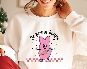 Könnte beinhalten: Weißer Pullover mit einem rosa Cartoon-Peep-Charakter, der ein Getränk hält und den Text "So peepin' boujee".