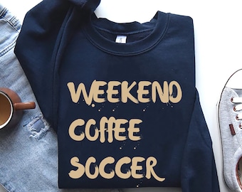 Puede incluir: Una sudadera azul marino con las palabras "Weekend Coffee Soccer" impresas en color tostado en la parte delantera.