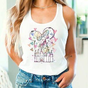 May include: A white tank top with a colorful illustration of a castle and Mickey Mouse ears with balloons. The castle is surrounded by stars and fireworks.