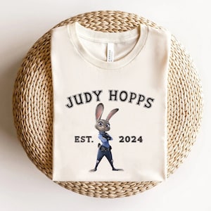 May include: A white t-shirt with a black graphic of Judy Hopps from the movie Zootopia. The graphic includes the text "Judy Hopps" and "Est. 2024".