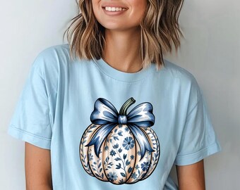 Könnte beinhalten: Hellblaues T-Shirt mit einem Kürbis-Design, verziert mit einer blauen Schleife und floralen Mustern. Der Text "COMFORT COLORS CHAMBRAY" ist oben im Bild aufgedruckt.