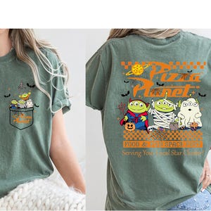 Pode incluir: Camiseta verde s&aacute;lvia com um design Pizza Planet com tema de Halloween. O bolso frontal tem um gr&aacute;fico de alien&iacute;genas. A parte de tr&aacute;s da camisa exibe o logotipo da Pizza Planet e alien&iacute;genas fantasiados, com o texto "FOOD & FUN SPACE BREW Serving Your Local Star Chaser!"