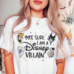 以下が含まれることがあります： 「99% Sure I Am A Disney Villain」の黒い文字が入った白いTシャツ。邪悪な女王、マレフィセント、アースラ、クルエラ・ド・ヴィルなど、ディズニーの悪役のイラストが描かれています。