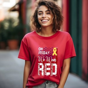 Może przedstawiać: Czerwona koszulka z przetartym wzorem amerykańskiej flagi i napisem "On Friday We Wear Red" z żółtą wstążką. Napis "Remember Everyone Deployed" jest napisany pionowo po lewej stronie flagi.