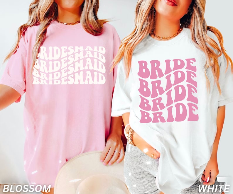 May include: Two t-shirts, one pink and one white, with a retro font design. The pink shirt says "BRIDESMAID" three times and the white shirt says "BRIDE" four times.