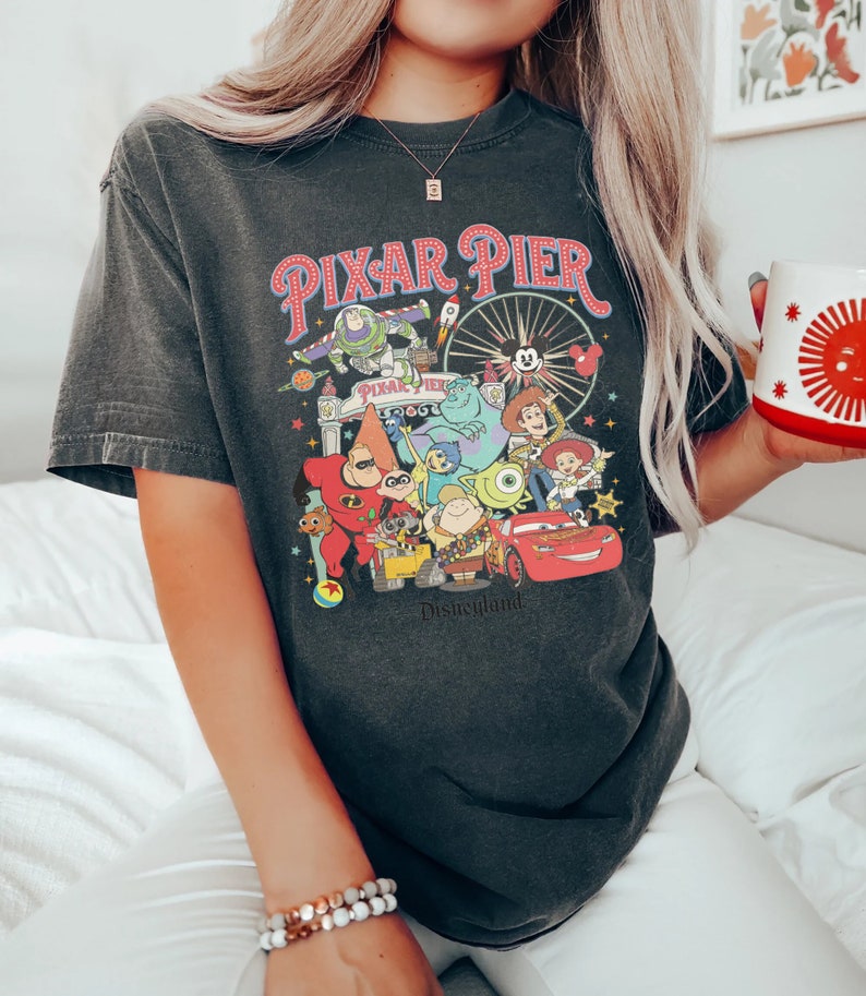 Puede incluir: Una camiseta negra con un gr&aacute;fico de estilo vintage de Pixar Pier en Disneyland. El gr&aacute;fico presenta personajes populares de Pixar como Buzz Lightyear, Woody, Mike Wazowski y Rayo McQueen. El texto "Pixar Pier" y "Disneyland" est&aacute;n incluidos en el gr&aacute;fico.