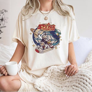 May include: A white t-shirt with a vintage-style graphic of a space mountain ride with the text "Space Mountain" printed on it.