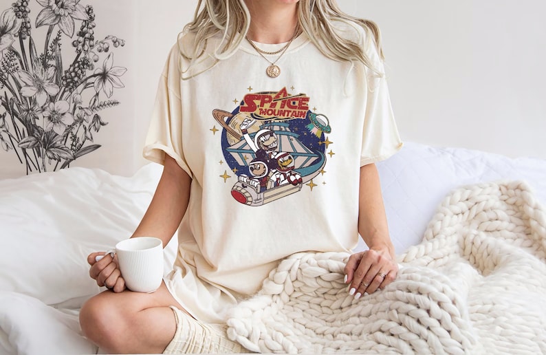 May include: A white t-shirt with a vintage-style graphic of a space mountain ride with the text "Space Mountain" printed on it.