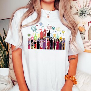 Puede incluir: Camiseta blanca con un gr&aacute;fico colorido de villanos de dibujos animados frente a torres de castillos. El dise&ntilde;o incluye fuegos artificiales y globos de Mickey Mouse. Una prenda casual para el d&iacute;a a d&iacute;a.